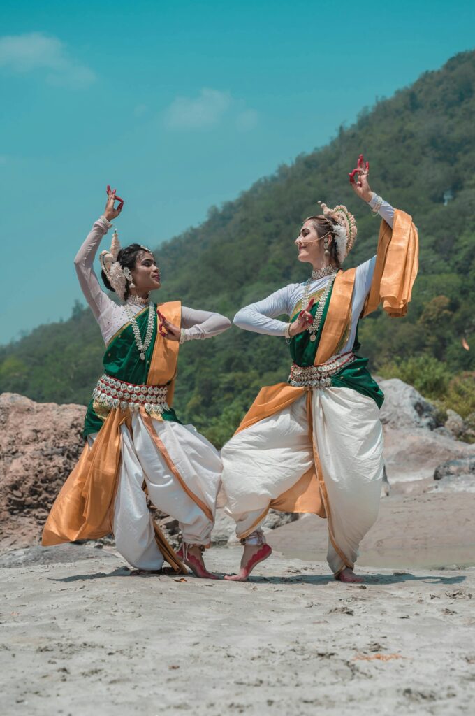 Two women in traditional Odissi dance attire performing on a scenic beach in Puri, India.