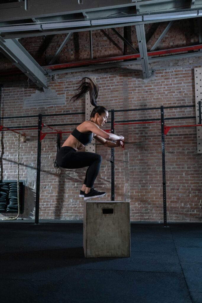 A fit woman executes a box jump in a gym setting, showcasing athleticism and fitness.