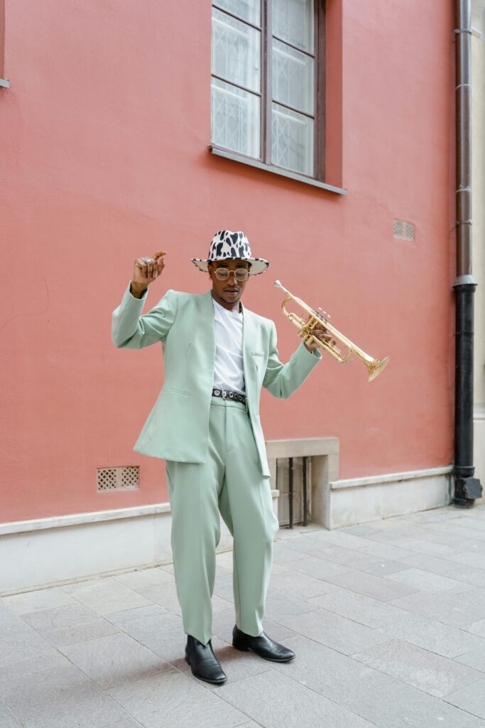 Fashionable street musician in mint suit playing trumpet against red wall outdoors.